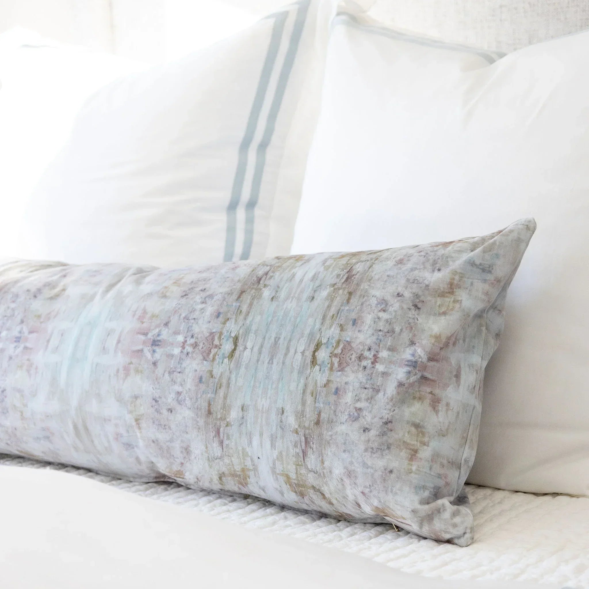 Luxury bolster pillow featuring an abstract garden-inspired pattern in layered bronze, iris blue, and earthy tones, styled for a collected modern traditional interior.